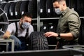salesman and customer in medical mask stand discussing car tires