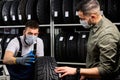 salesman and customer in medical mask stand discussing car tires