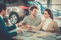 Salesman giving the key of the new car to a young couple at the dealership showroom. Royalty Free Stock Photo