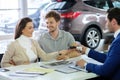 Salesman giving the key of the new car to a young couple at the dealership showroom. Royalty Free Stock Photo