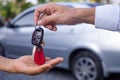 The salesman is handing over the car keys to the hand of a female customer. After signing the contract between purchase - sale suc