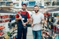 Salesman and bearded client posing with giant wrenches in power tools store.