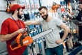Salesman is showing bearded client new chainsaw in power tools store.