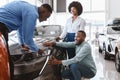 Salesman talking to young black couple, showing them new luxury car at auto dealership Royalty Free Stock Photo