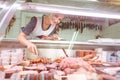 Saleswoman in butchery behind glass display with meat and sausages