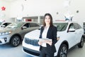 Saleswoman Holding Clipboard By Car In Showroom