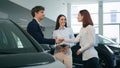 Saleswoman woman dealer seller trader female showing new vehicle to customers happy couple buying car automobile salon Royalty Free Stock Photo