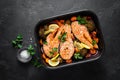 Salmon. Baked salmon fish steaks with vegetables, broccoli, carrot and onion on black background