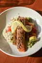 salmon entree with risotto, vegetables, and a lemon wedge photographed from above on a round white plate