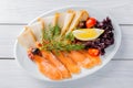 Salmon fillet pieces, sturgeon pieces served with lemon, black olives, herbs, cherry tomato and pomegranate seeds on white plate a Royalty Free Stock Photo