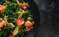 Salmon Kale super food Salad with avocado, pistachio nuts and blueberries on black plate