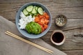 Salmon poke bowl with fresh fish, rice, cucumber, avocado with black and white sesame. Old wooden table. Food concept Royalty Free Stock Photo