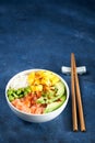 Salmon Poke bowl Raw fish salad Asian trendy food, mango, soy beans edamame, rice, avocado, served in bowl, chopsticks, blue dark Royalty Free Stock Photo