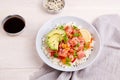 Salmon poke bowl with rice, avocado, micro greens, pepper and soy sauce on white wooden background. Royalty Free Stock Photo