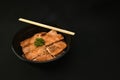 Salmon on rice looks appetizing in a black bowl.