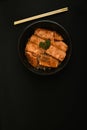 Salmon on rice looks appetizing in a black bowl.