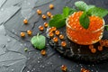 Salmon roe in glass bowl with fresh mint, textured black background
