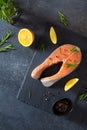 Salmon steak raw fish with ingredients prepared for cooking. Fresh trout steak with lemon, salt, pepper and rosemary on dark stone Royalty Free Stock Photo