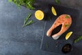 Salmon steak raw fish prepared for cooking. Fresh trout steak with salt, pepper, lemon and rosemary on black slate board on dark Royalty Free Stock Photo