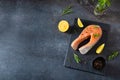 Salmon steak raw fish prepared for cooking. Fresh trout steak with salt, pepper, lemon and rosemary on black slate board on dark Royalty Free Stock Photo