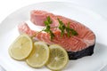 Salmon steak with a sprig of parsley and three lemon slices on a white plate