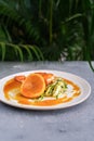 Salmon steak with zucchini noodles with orange sauce and orange on a white plate