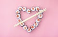 Salmon sushi rolls laid out in the shape of a heart on a pink background. The concept of Japanese cuisine for Valentine`s Day,