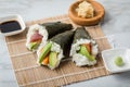 Salmon, tuna fish and Surimi avocado Temaki sushi with soy sauce, pickled ginger and wasabi on mat and marble background Royalty Free Stock Photo