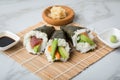 Salmon, tuna fish and Surimi avocado Temaki sushi with soy sauce, pickled ginger and wasabi on mat and marble background Royalty Free Stock Photo