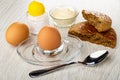 Salt, bowl with mayonnaise, rye bread, brown egg on egg stand, spoon on wooden table Royalty Free Stock Photo