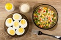 Salt, bowl with mayonnaise, saucer with halves boiled eggs, bowl with vegetable mix, fork on table. Top view