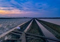 Salt farm in the morning with sunrise sky and clouds. Landscape of sea salt field in Thailand. Sea water in canal and soil pathway Royalty Free Stock Photo