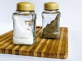 Salt and pepper in a glass shaker and pepper shaker stand on a cutting board