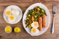 Salt, pepper shakers, plate with vegetable mix, egg, fried sausages, plate with halves egg, fork on table. Top view Royalty Free Stock Photo