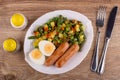 Salt shaker, pepper shaker, plate with vegetable mix, egg, fried sausages, fork, knife on table. Top view Royalty Free Stock Photo