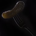 Salted cucumber on a fork on a black background