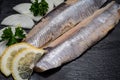 Salted Deboned Herring Fillets garnished with Yellow Onion, Lemon, Fresh Parsley and Peppercorns. Natural black stone . Royalty Free Stock Photo