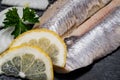 Salted Deboned Herring Fillets garnished with Yellow Onion, Lemon, Fresh Parsley and Peppercorns. Natural black stone . Royalty Free Stock Photo