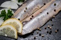 Salted Deboned Herring Fillets garnished with Yellow Onion, Lemon, Fresh Parsley and Peppercorns. Natural black stone . Royalty Free Stock Photo