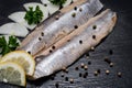 Salted Deboned Herring Fillets garnished with Yellow Onion, Lemon, Fresh Parsley and Peppercorns. Natural black stone . Royalty Free Stock Photo