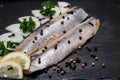 Salted Deboned Herring Fillets garnished with Yellow Onion, Lemon, Fresh Parsley and Peppercorns. Natural black stone . Royalty Free Stock Photo