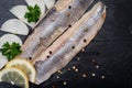 Salted Deboned Herring Fillets garnished with Yellow Onion, Lemon, Fresh Parsley and Peppercorns. Natural black stone . Royalty Free Stock Photo