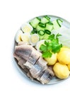 Salted herring with boiled potatoes and quial eggs on a white plate isolated on white