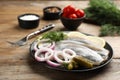 Salted herring fillets served with onion, pickles, dill and lemon on wooden table