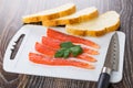 Salted salmon, parsley on cutting board, pieces of bread, knife