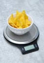 Salted tortilla nacho chips in a white bowl on a kitchen scale, grey marble table