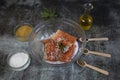 Salting salmon at home, fillet in a transparent bowl olive oil and spices in wooden spoons on the tabl Royalty Free Stock Photo