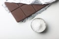 Salty chocolate and a bowl of sea salt on white background flat lay