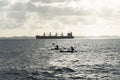 People in two kayaks sailing in the bay of all saints next to a large ship