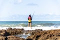 Fisherman woman with fishing rod on the rocks fishing on the beach